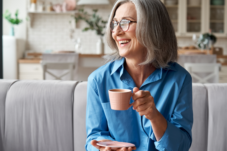 Senior woman enjoying her morning coffee on a couch, bathed in natural sunlight, symbolizing a relaxed approach to monitoring blood pressure.