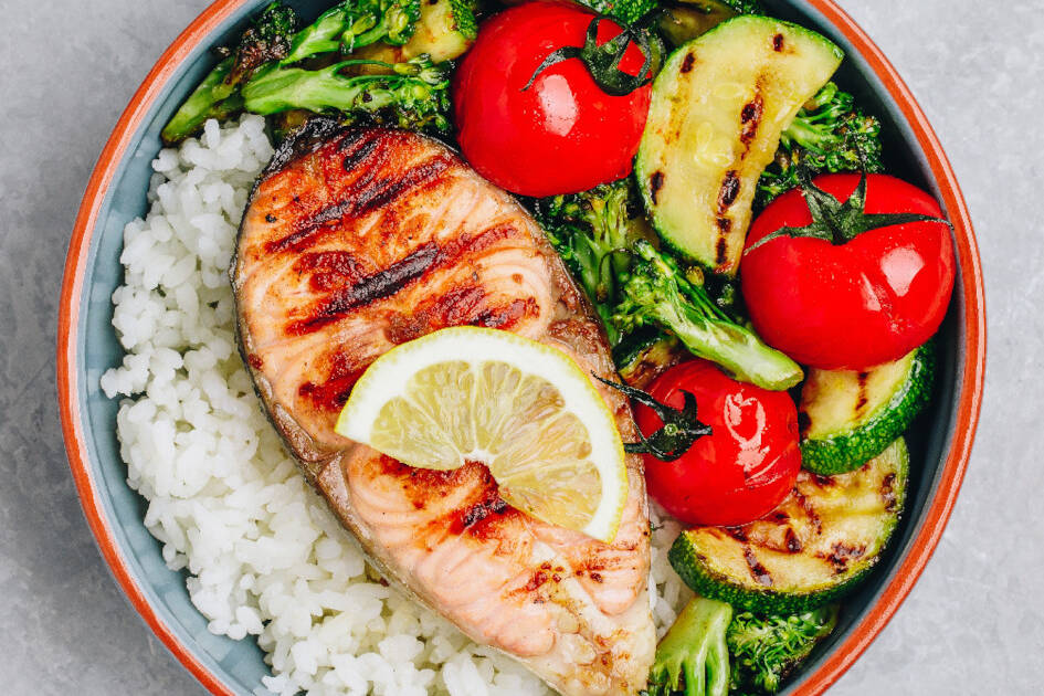 A nutritious meal showcasing the Mediterranean diet with white rice, grilled salmon, slices of avocado, tomato, and cucumbers on a plate.